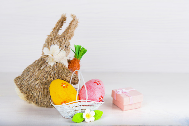 Wicker Easter bunny with Easter eggs in basket on white wooden b - Фото, зображення