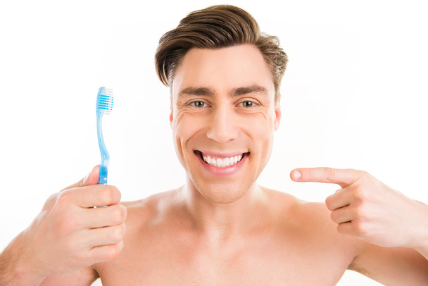 Toothy happy young man pointing on blue toothbrush - Foto, afbeelding