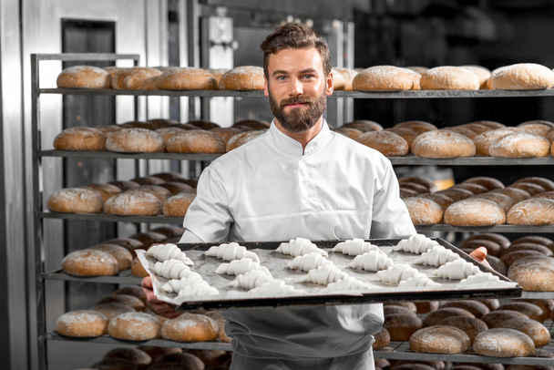 Красивый пекарь держит поднос, полный свежеиспеченных круассанов
 - Фото, изображение