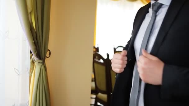 Aantrekkelijke ernstige jonge man omhoog het kleden van zijn fashinable zwart-pak voor het raam. - Video
