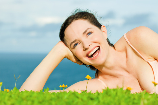 A zöld fűben fekvő gyönyörű boldog nő nevetve - Fotó, kép