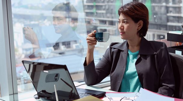 Femme d'affaires dans le bureau avec vue sur la fenêtre et tasse de café sa main
 - Photo, image