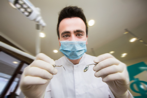 young men dentist with sterile mask readily approaching a patient with dental instruments held in the hands protected with surgical gloves young dentist with sterile mask - Foto, imagen