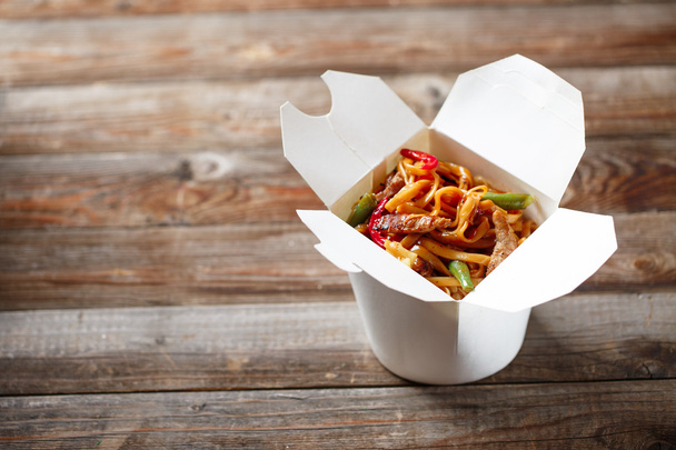 Noodles with pork and vegetables in take-out box on wooden table - Zdjęcie, obraz