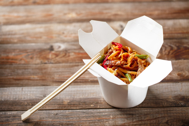 Noodles with pork and vegetables in take-out box on wooden table - Foto, imagen