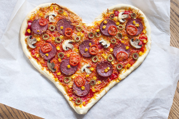 Baked heart-shaped homemade pizza topped with mozzarella and tomato slices, with salami, pepperoni, mushrooms, olives and garlic close-up. - Fotoğraf, Görsel
