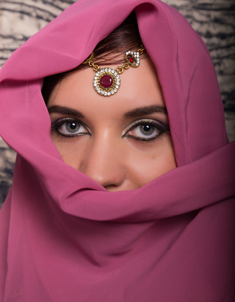 Closeup of beautiful young woman with oriental make-up and shawl over her head. caucasian woman dressed in oriental style - Фото, изображение