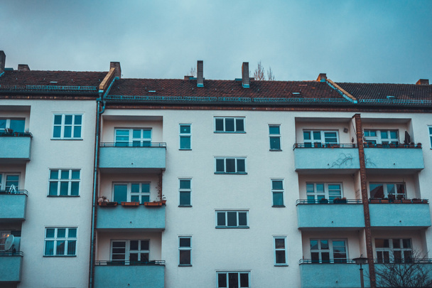 Row of apartment buildings with white walls and balconies in simple architectural design under overcast sky - Fotografie, Obrázek