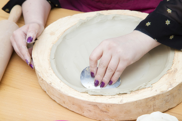 Mani di donna con strumento metallico che fa un piatto di argilla bianca
 - Foto, immagini