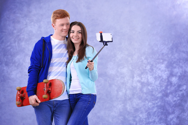 Teenager couple with skateboard using stick for photo by their self on grey background - Zdjęcie, obraz