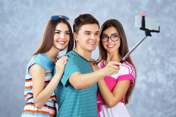Teenager friends making photo by their self with mobile phone on grey background on grey background - Foto, Bild