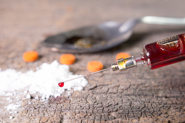 Drug syringe with blood, amphetamine tablets and cooked heroin in spoon. on old wood background - Photo, Image