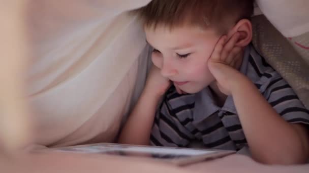Menino deitado sob cobertor e assistindo desenhos animados no touch pad
 - Filmagem, Vídeo