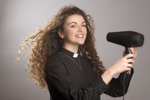 Jeune vicaire utilisant un sèche-cheveux pour sécher ses cheveux longs
 - Photo, image