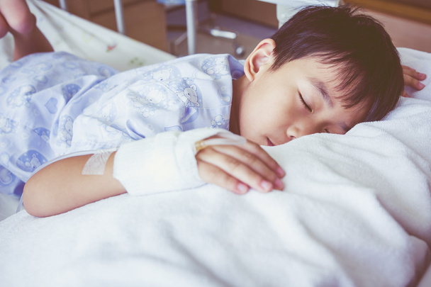 Азиатский мальчик спит на больничном, физраствор внутривенно (IV) под рукой
. - Фото, изображение