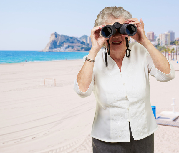 Portrait of senior woman looking through a binoculars in the bea - Photo, Image