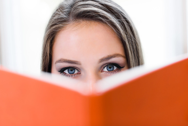 Beautiful blonde student girl covering her face behind the orange book. - Foto, Bild
