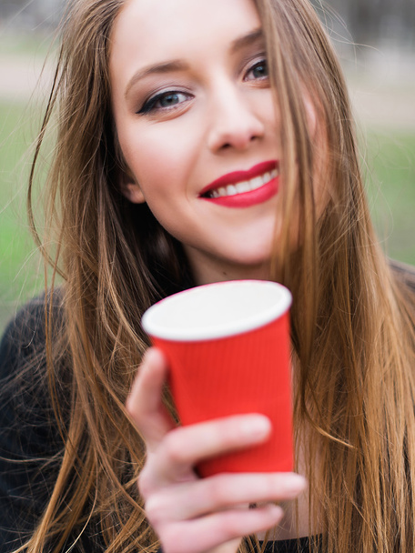 Portrait of young beautiful stylish girl drinking coffee in the park - 写真・画像
