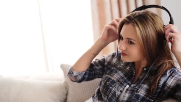 Jonge mooie vrouw liggend op de Bank en het luisteren van muziek in haar koptelefoon op de woonkamer. - Video