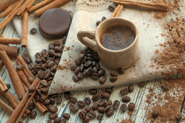 A composition with a handmade earthenware cup of coffee, cinnamon stickss, coffee beans, cocoa powder and a chocolate candy - Fotoğraf, Görsel
