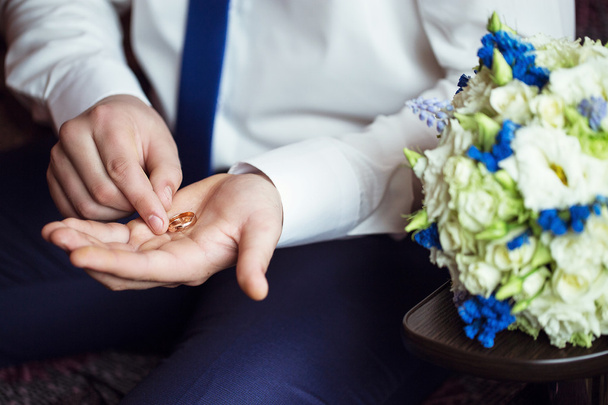 wedding rings in the hand of the groom near to wedding bouquet - Photo, Image