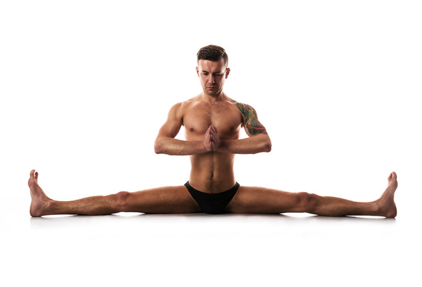 young strong man doing yoga and gymnastics, cross-twine. - Foto, Imagen