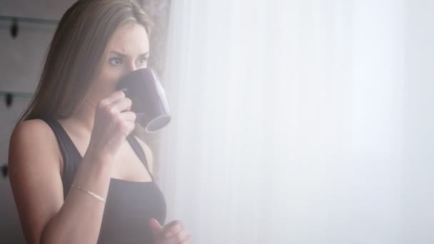 Atraktivní mladá dáma oddechuje a pití šálku čaje nebo kávy před okno doma. - Záběry, video