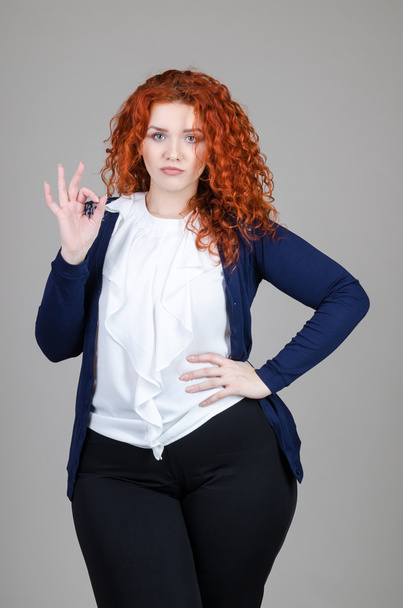 beautiful fat girl with red hair in a business suit on a gray background - Valokuva, kuva