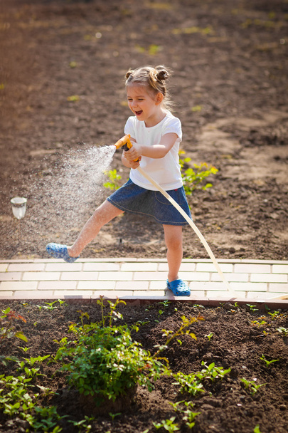 Забавна дитина поливає квіти в саду
 - Фото, зображення