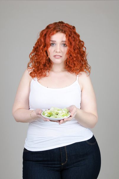 beautiful fat girl with red hair with a plate of salad in hand on gray background - Fotoğraf, Görsel