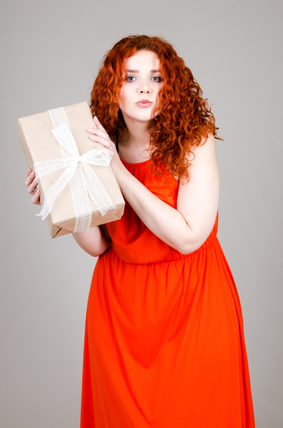 beautiful fat girl with red hair with a gift box in hand on gray background - Foto, afbeelding