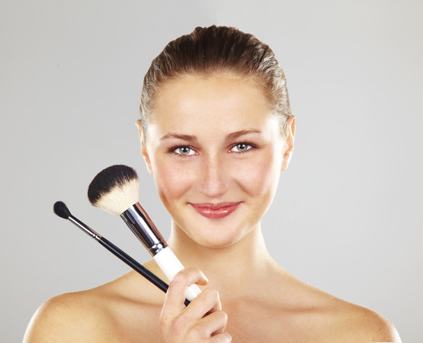 Beautiful young woman smiling holds the make-up brushes. Fashion model posing over white background - Photo, Image