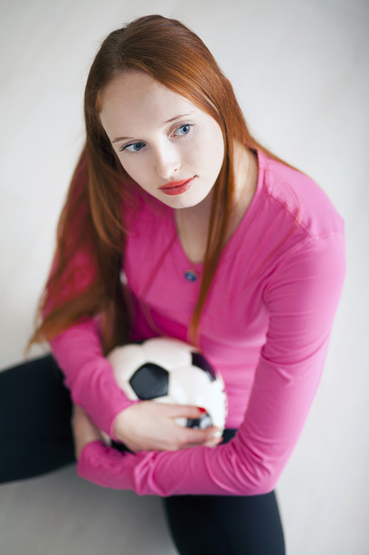 Atractiva chica rubia sosteniendo una pelota de fútbol y sentada en el suelo
 - Foto, imagen