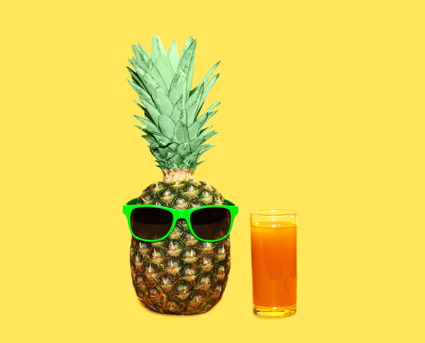 Pineapple with sunglasses and glass fruit juice on yellow backgr - Фото, зображення