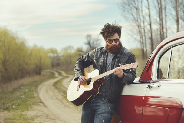 Bearded man playing guitar outdoors near retro car - Photo, image