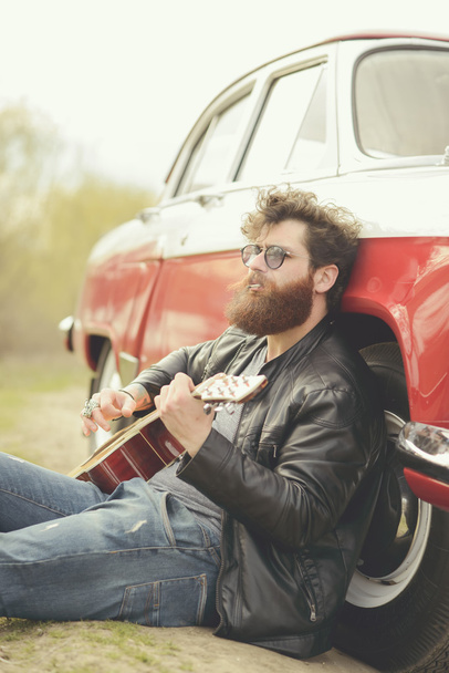 Bearded man playing guitar outdoors near retro car - Zdjęcie, obraz