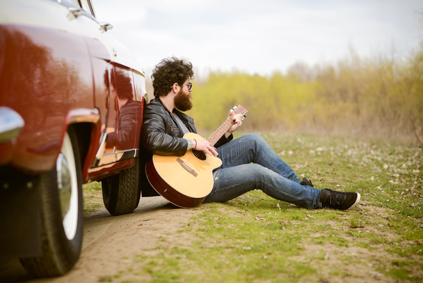レトロな車の屋外近くギターを弾くひげを生やした男 - 写真・画像