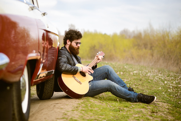 Bearded man playing guitar outdoors near retro car - Photo, image