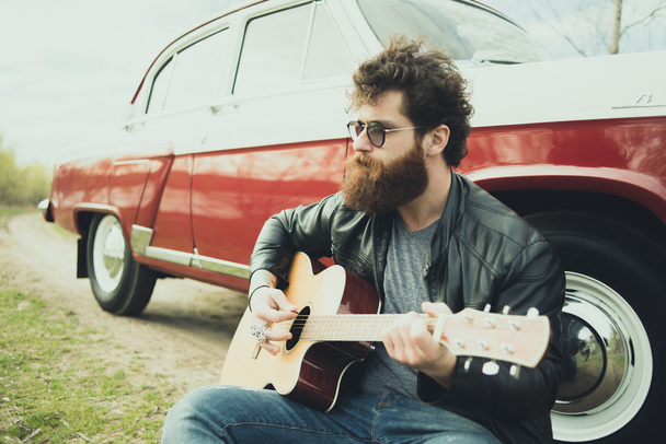 Bearded man playing guitar outdoors near retro car - Foto, afbeelding
