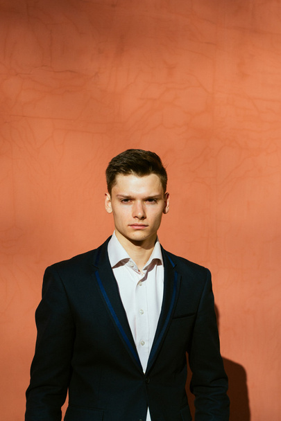 young man in a black suit on a background of a orange wall - Фото, изображение
