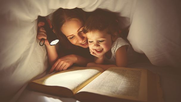 Οικογενειακή ανάγνωση τον ύπνο. Μαμά και παιδί ανάγνωση βιβλίων με ένα flashl - Φωτογραφία, εικόνα