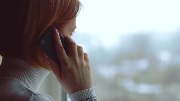 Vrouw praten met haar moeder aan de telefoon kijkt uit het raam - Video