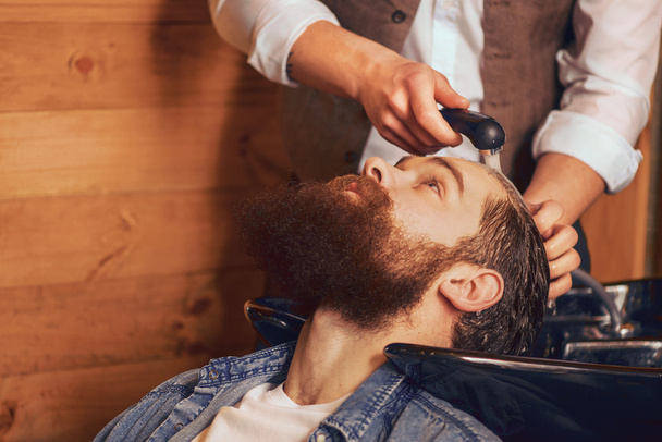 Barber washing head of bearded man - Fotó, kép