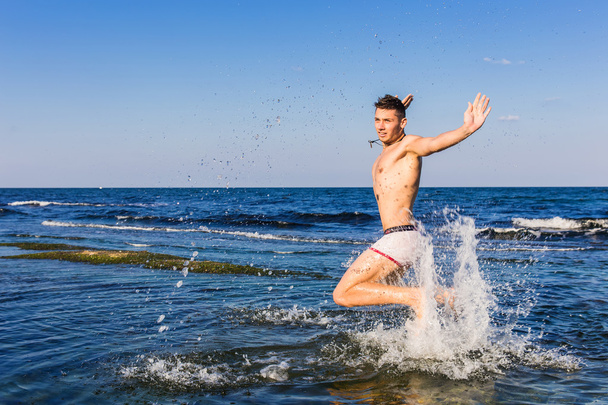Nackter junger Mann springt vor Freude aus dem Wasser - Foto, Bild