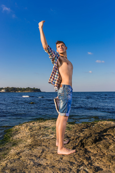 Atractivo joven moda sexy hombre en la roca cerca del agua de mar
 - Foto, Imagen