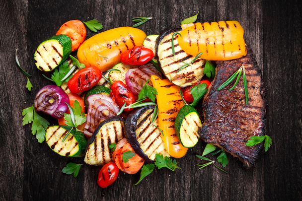 Beef steak and Grilled vegetables. On cutting dark board background - Photo, Image