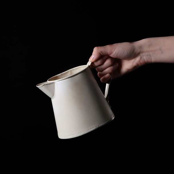 Female hand holding white plastic jug on black background - Foto, Bild