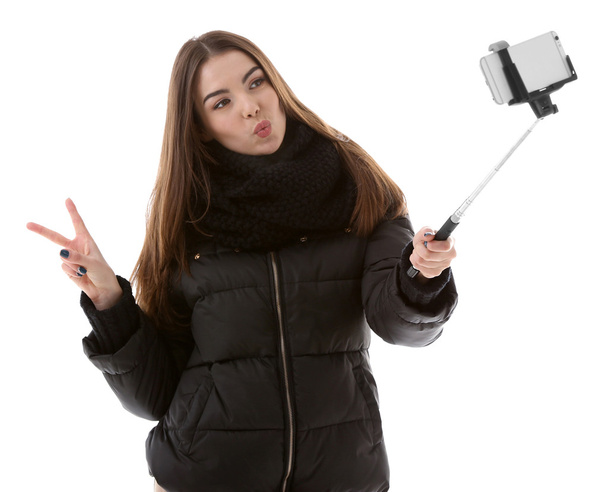 Young attractive girl in winter clothing making photo by her self with mobile phone, isolated on white - Valokuva, kuva