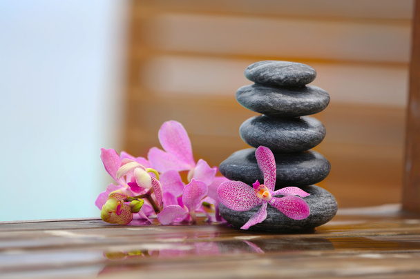 Stack of spa stones with pink orchids on wooden wet bridge - Foto, Imagem