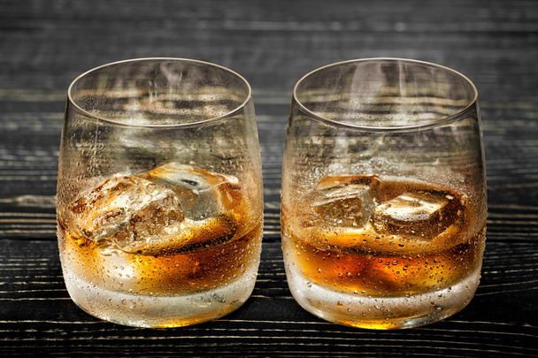Whiskey met ijs op een zwarte houten achtergrond - Foto, afbeelding